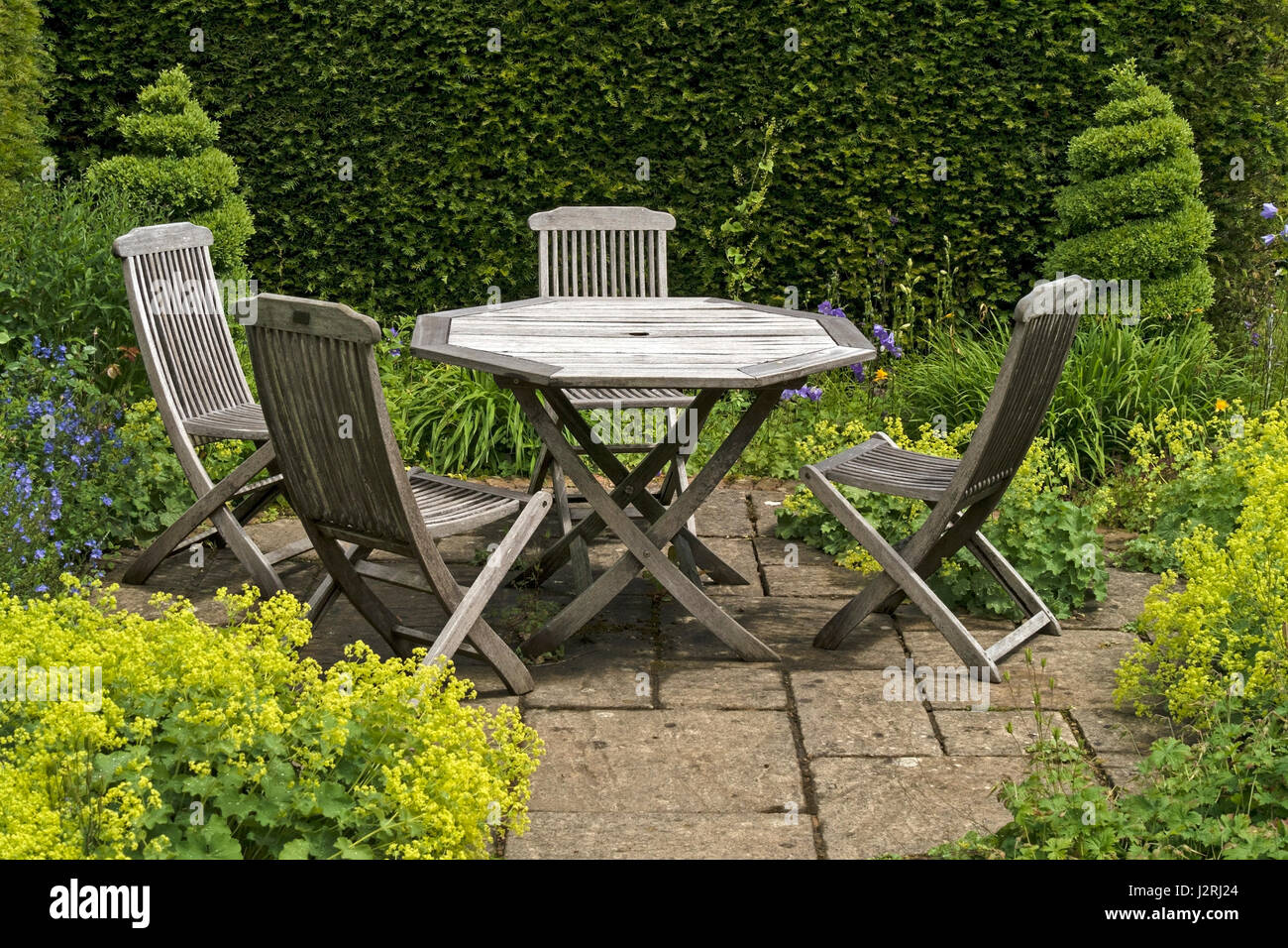 Holztisch mit vier Stühlen auf kleine zerschlug Gartenterrasse mit grünen Grenzen und Formschnitt durch Barnsdale Gärten, Rutland, England, UK Stockfoto