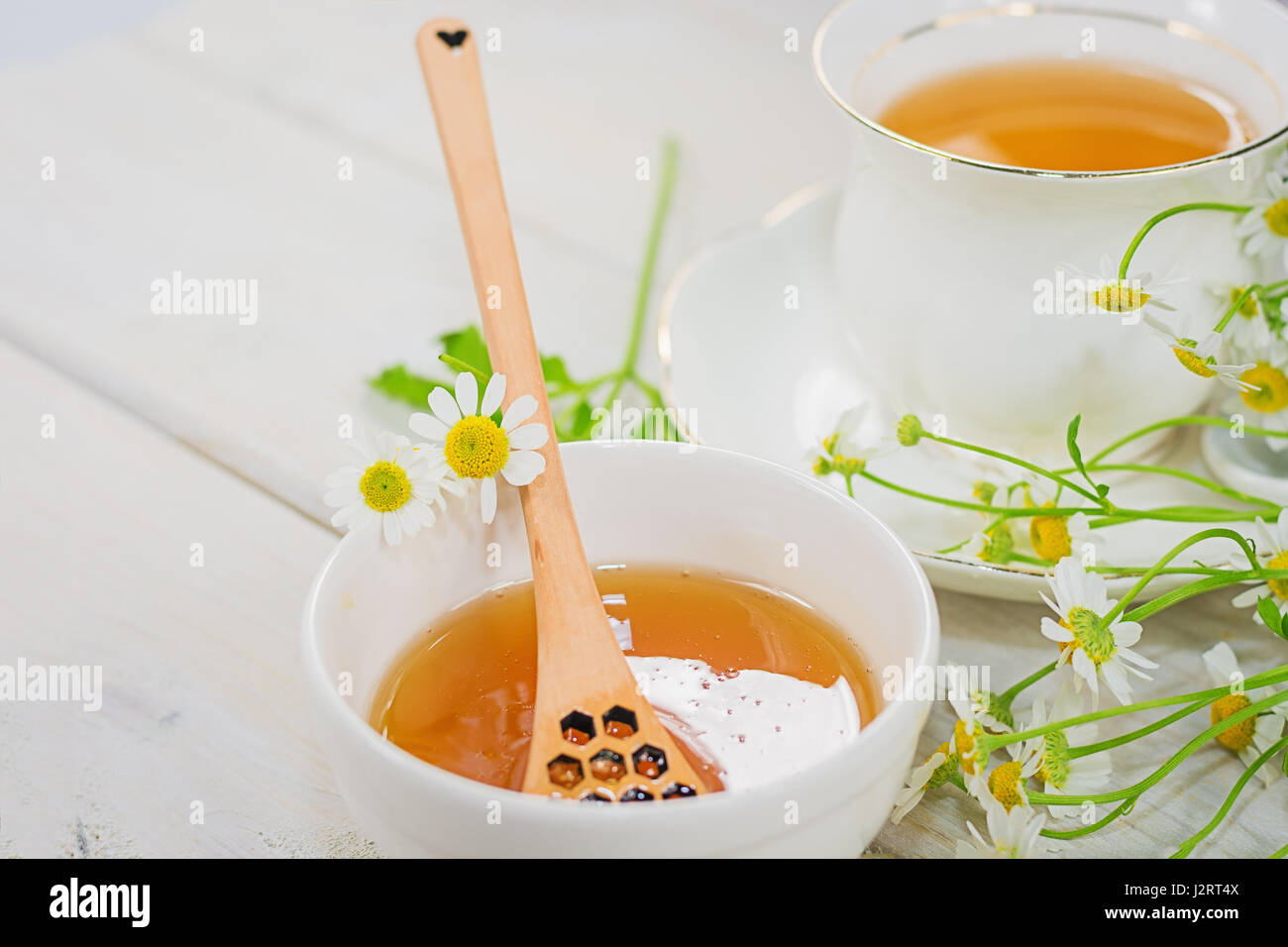 Schale mit Blütenhonig und Löffel mit einer Tasse Tee, dekoriert mit Kamille gefüllt Stockfoto