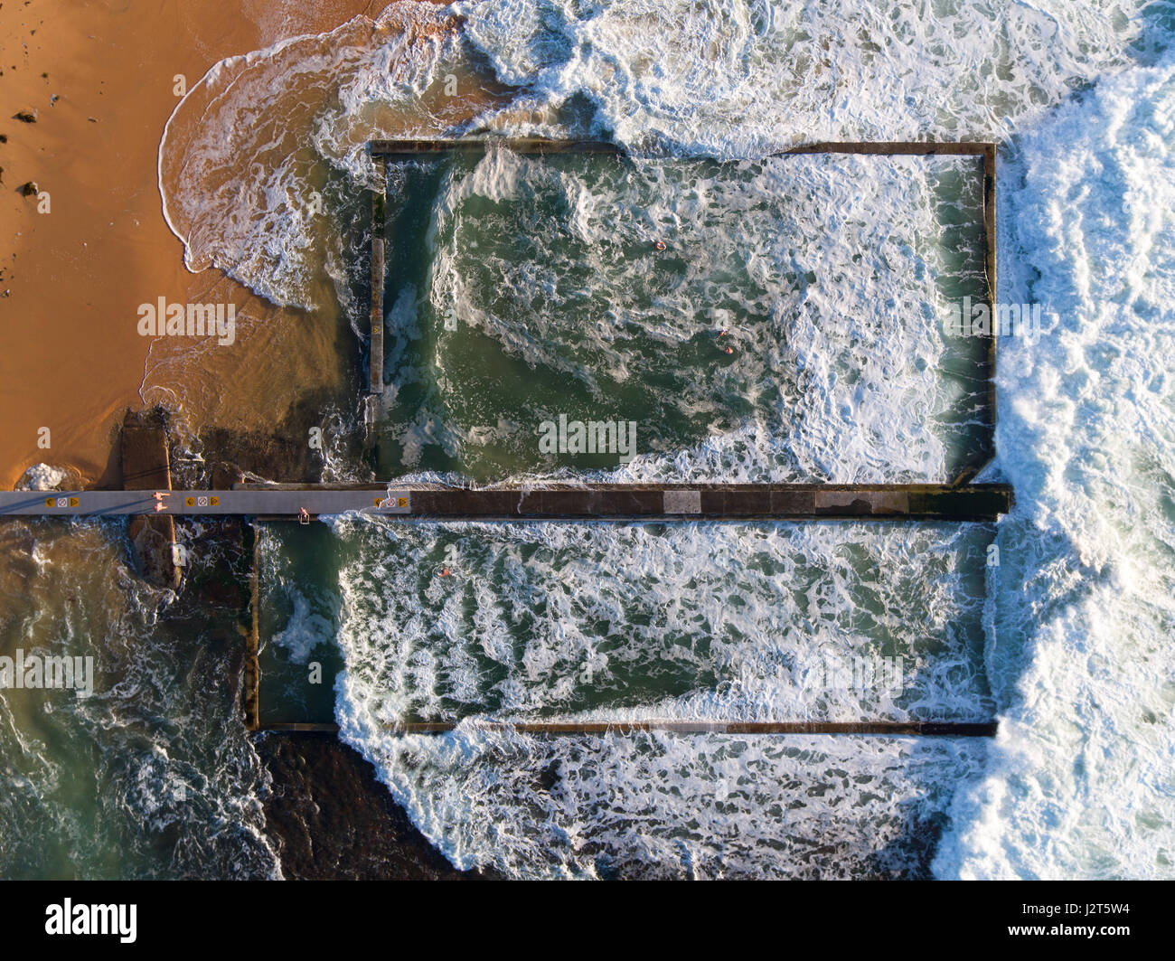 VERTIKALE LUFTAUFNAHME. Schwimmer in der Sicherheit eines Steinpools aus einem rauhen Meer. Austinmer, New South Wales, Australien. Stockfoto