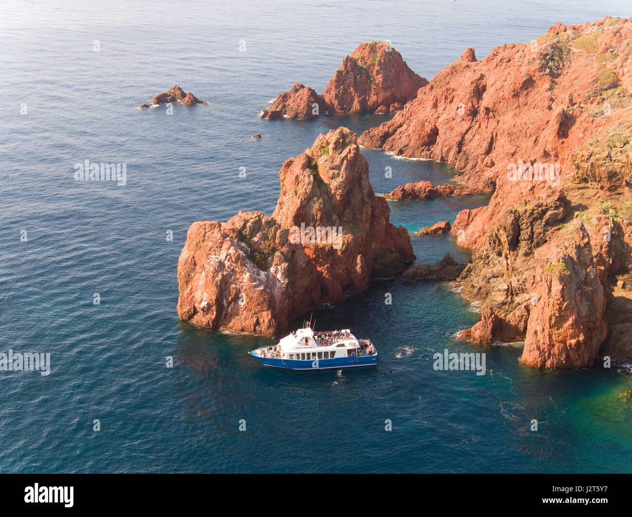 LUFTAUFNAHME. Touristen auf einem Sightseeing-Boot bewundern den spektakulären roten Felsen des Cap du Dramont. Saint-Raphël, Var, Französische Riviera, Frankreich. Stockfoto