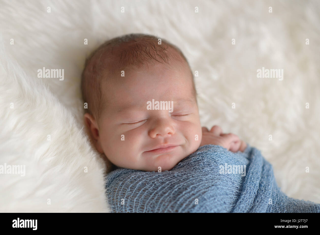 Schlafen, neun Tage alten, neugeborenes Baby Boy mit einem Lächeln auf  seinem Gesicht. Er ist in einer leichten blauen Packung gepuckt. Gedreht im  Studio auf einem weißen, Schaffell-Teppich Stockfotografie - Alamy