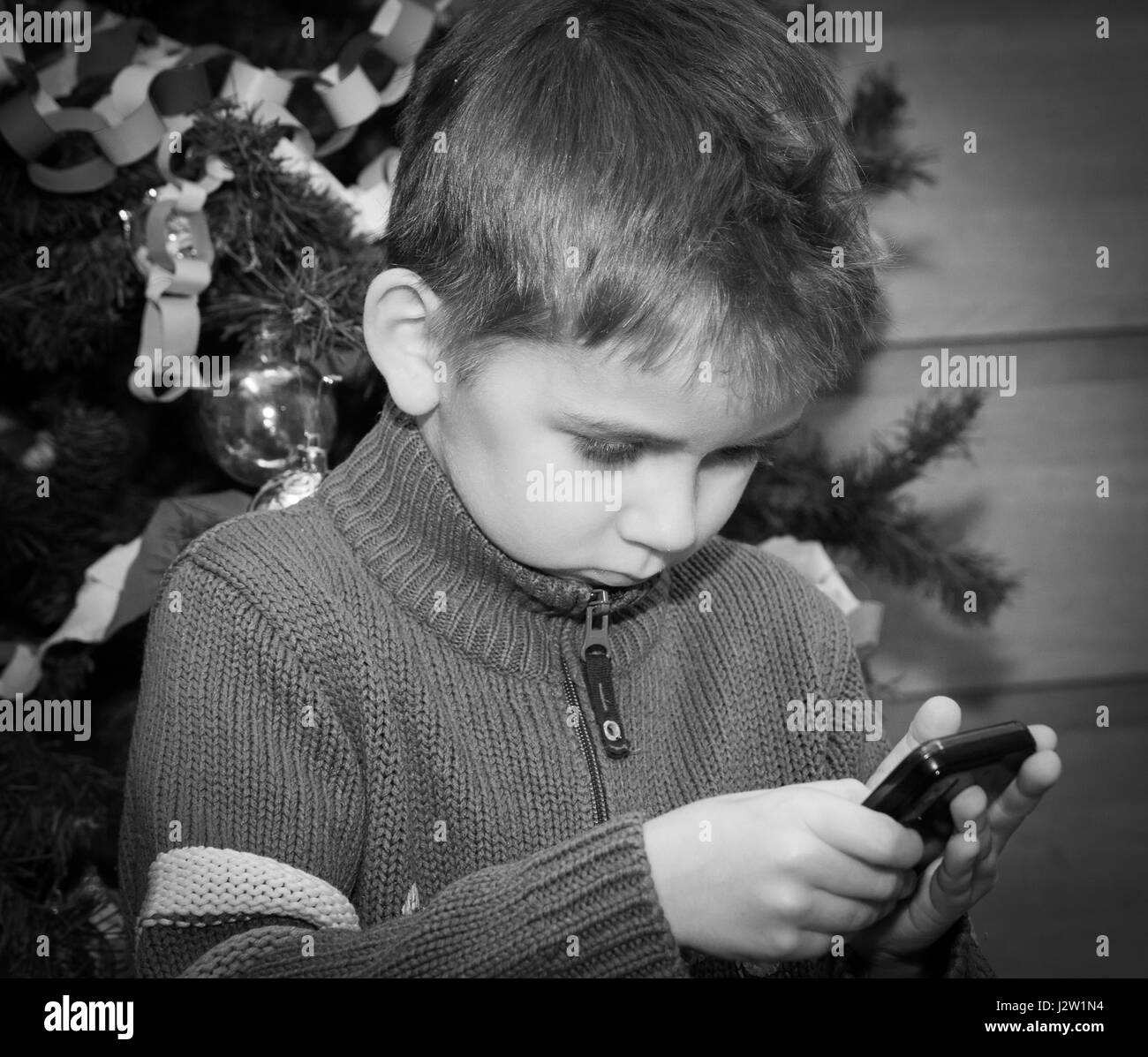 Ein kleiner blonder Junge sitzt unter einem Weihnachtsbaum und Geschenke warten. Stockfoto