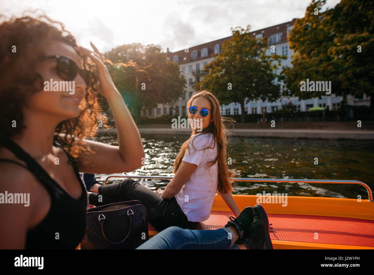 Schuss der lächelnde junge Frau sitzt auf dem Deck des Bootes mit Freundin vor. Zwei junge Frauen auf Boot in See. Stockfoto