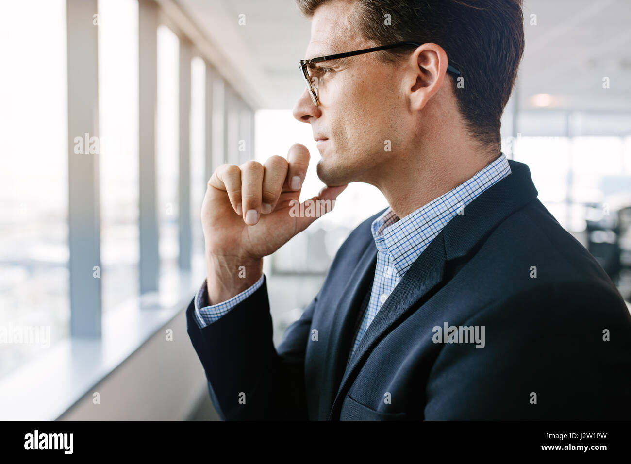 Richtungskontrolle Ansicht von reifer Geschäftsmann neben Office-Fenster nach draußen und denken mit Hand am Kinn. Stockfoto