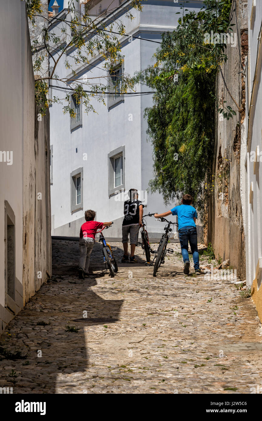 drei Jungs schieben ihre Räder auf einer Straße in Tavira, Portugal Stockfoto