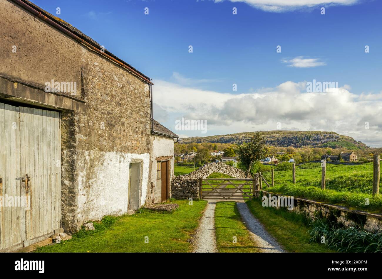 Eine alte Scheune in Cumbria an einem sonnigen Tag mit einem Holztor und entfernten Hügel. Stockfoto