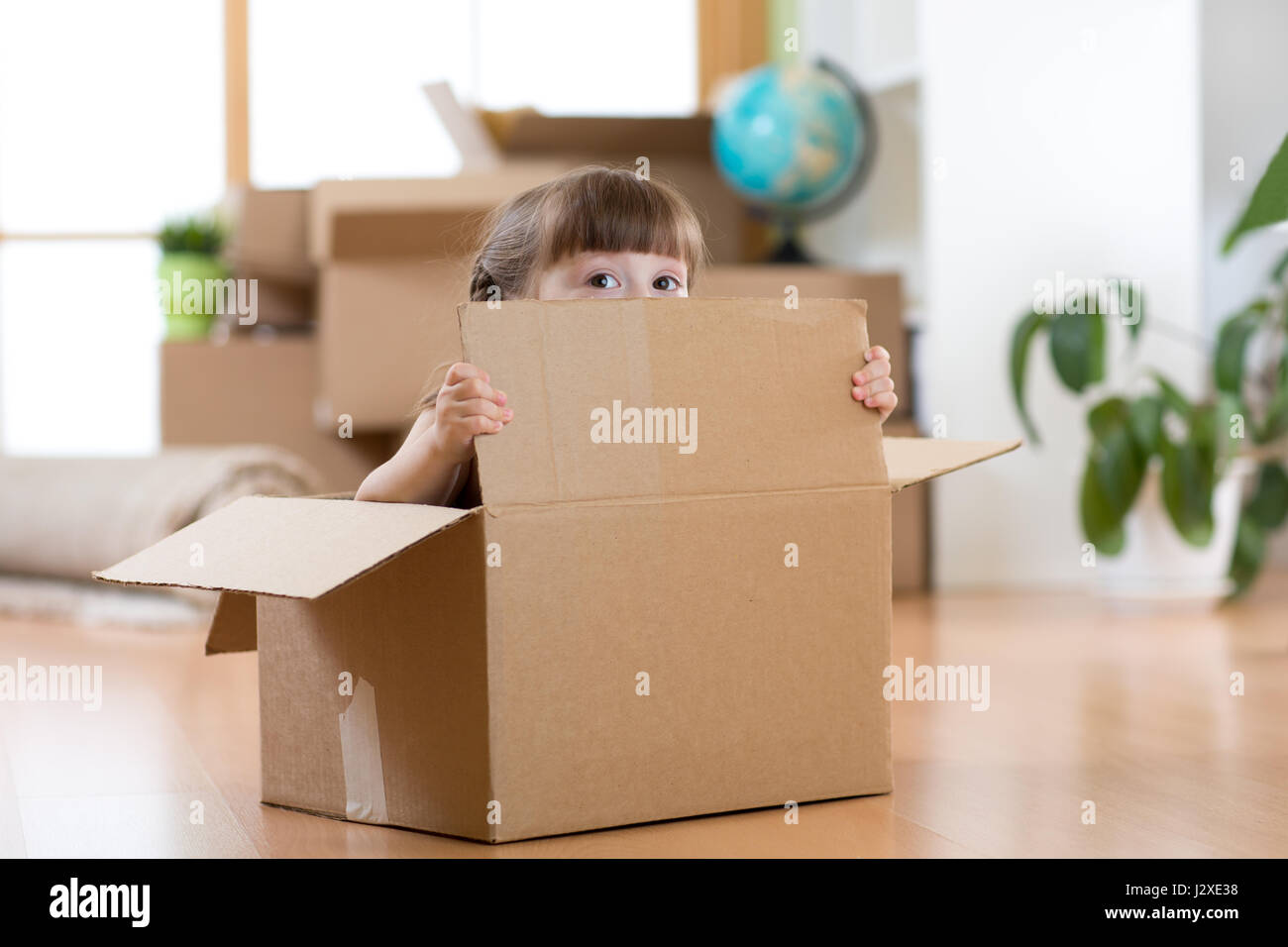 hübsches Kind sitzt in einem Karton nach dem Umzug in neue Wohnung Stockfoto