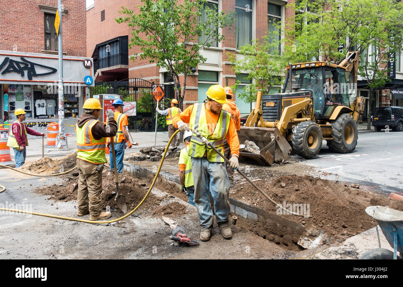 Eine Gruppe von Bauarbeitern, die Reparatur der unterirdischen Infrastruktur in einer Straße von Soho in New York. Mann im Vordergrund hält ein Druckluftschlauch. Stockfoto