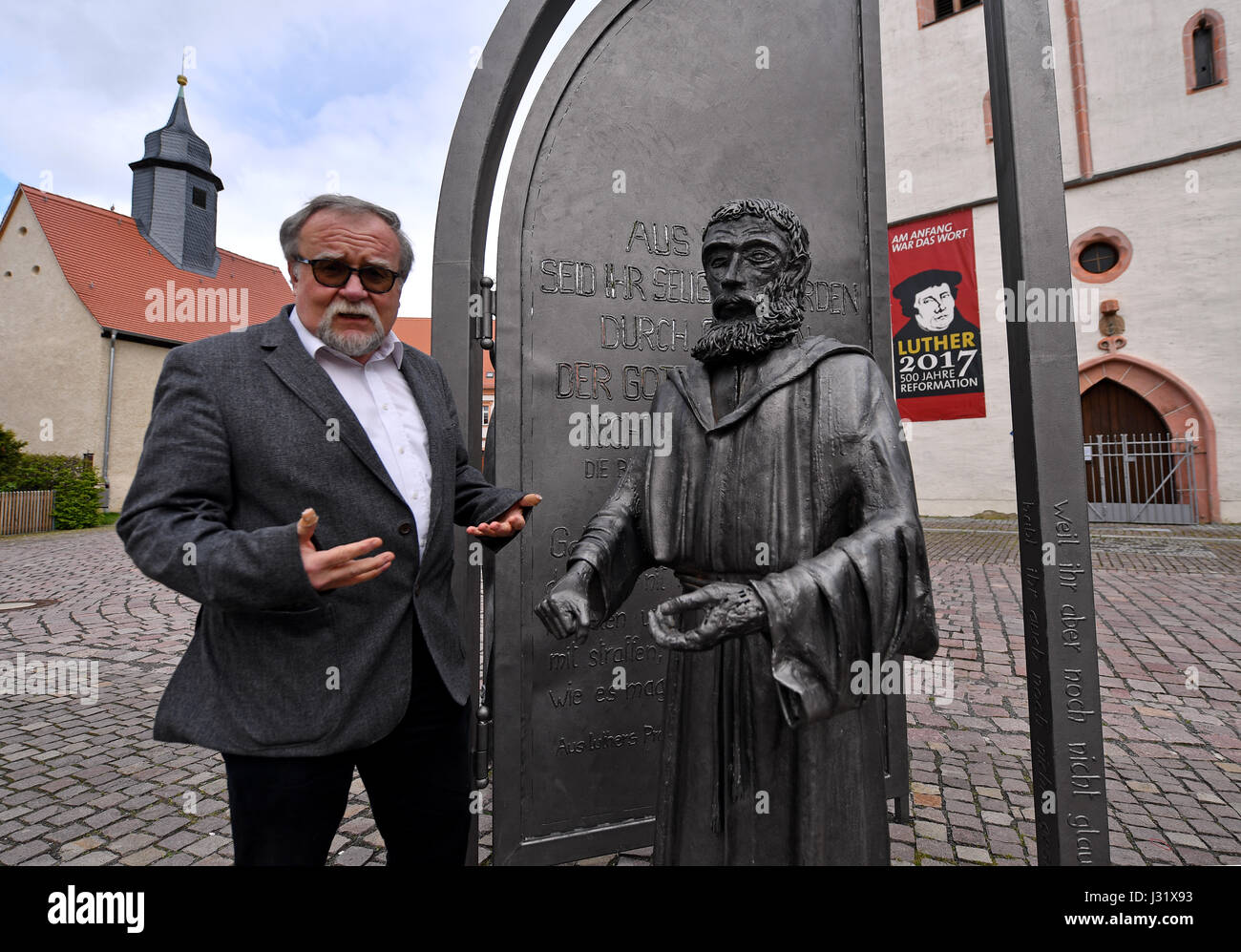 Borna, Deutschland. 19. April 2017. Dekan Matthias Weismann stehend nahe bei einem Denkmal von Martin Luther als Junker Jörg auf dem Martin Luther Platz in Borna, Deutschland, 19. April 2017. In der Mitte des Platzes ein Denkmal ist eine Hommage an Luthers Aufenthalte in Borna zwischen Emmauskirche Chruch (l.) und die Stadt von St. Marien. Foto: Hendrik Schmidt/Dpa-Zentralbild/Dpa/Alamy Live News Stockfoto