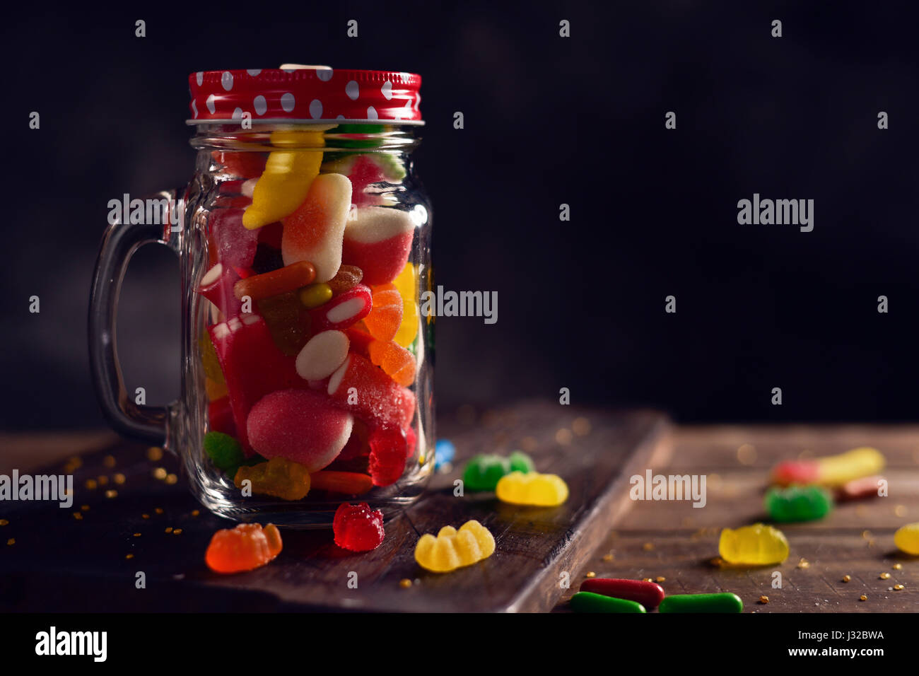 ein Einmachglas voller Bonbons mit verschiedenen Geschmacksrichtungen und Farben auf einem rustikalen Holztisch Stockfoto
