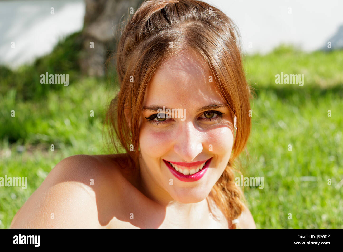 Schöne junge Frau mit grünen Augen Lächeln, Kamera, während ist auf dem Rasen liegen. Stockfoto