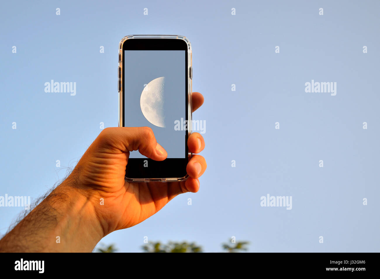 Hand des Mannes eine Aufnahme des Mondes auf einem blauen Himmel während des Tages mit einem smartphone Stockfoto