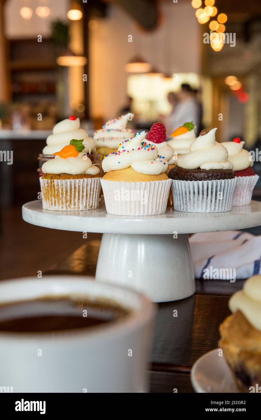 Gourmet-assorted Muffins angezeigt auf einem weißen Keramik Kuchen stehen in einer Bäckerei Stockfoto