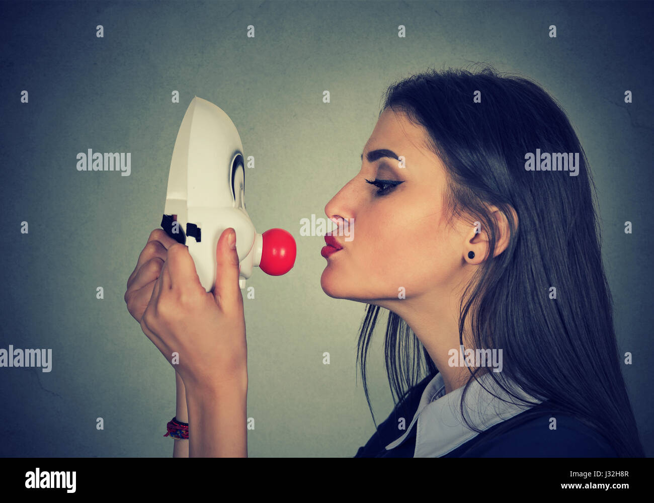 Frau küssen Clownsmaske auf graue Wand Hintergrund Stockfoto
