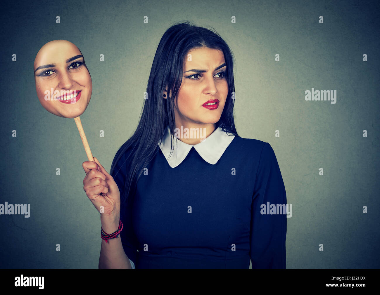 Junge Frau mit angewidert traurigen Ausdruck hält eine Maske mit dem Ausdruck ihrer Fröhlichkeit Stockfoto