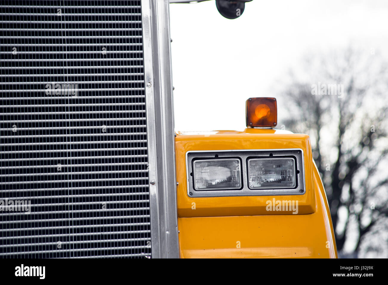 Detail der Scheinwerfer und Kühlergrill des gelben Sattelschlepper auf dem Baum-Hintergrund Stockfoto