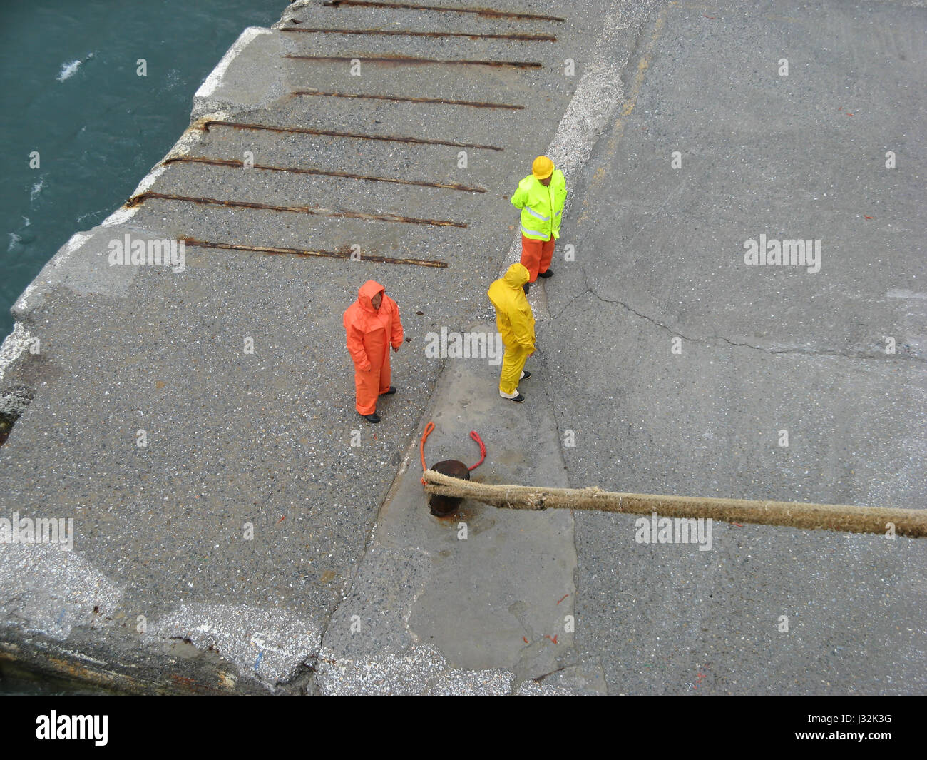 Insel Andros, Kykladen, Griechenland - drei Männer in Feuchtarbeit schützende passen stehend auf der Anklagebank warten auf Erlaubnis, um Schiff festmachen Seile freizugeben Stockfoto