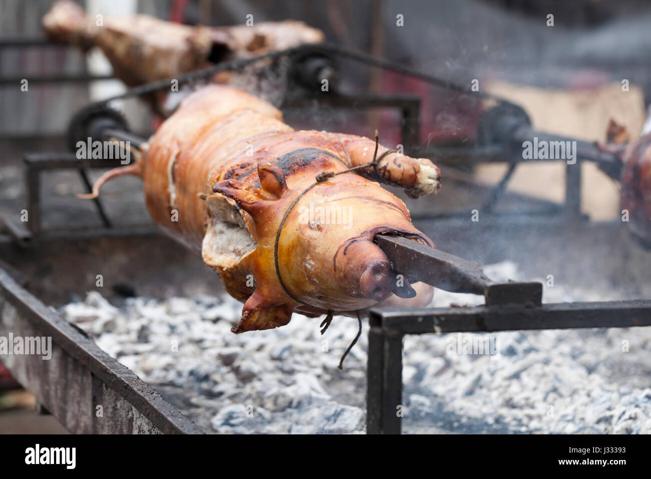 Traditionell Spanferkel auf einer sich drehenden Spieß mit Feuer und Rauch. Sehr leckeres Essen. Stockfoto