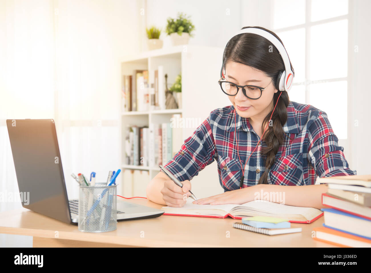 Porträt eines Schülers auf Linie mit Kopfhörer und Laptop Notizen in einem Notizbuch sitzt an ihrem Schreibtisch zu Hause lernen. Gemischte Rassen asiatische chinesische mod Stockfoto