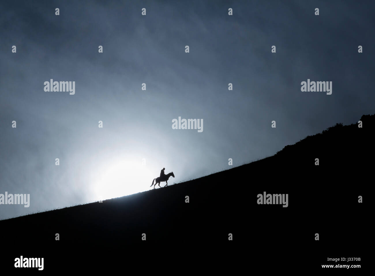 Einsame Reiter klettern auf Berge fahren gegen die Sonne Silhouette Stockfoto