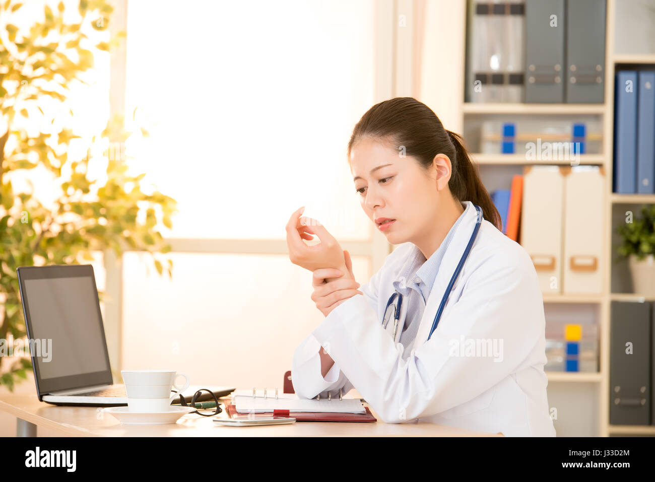 Blick auf eine junge Ärztin mit Handgelenk Schmerzen in Klinik-Büro. Gemischte Rassen asiatische chinesische Modell. Ärzte und medizinisches Konzept. Stockfoto