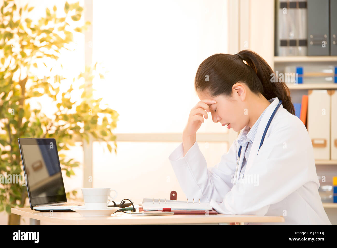 Arzt bekam Migräne überarbeitet und gestresst. Medizinisches Fachpersonal in Laborkittel tragen Stethoskop im Krankenhaus. Gemischte Rassen asiatische chinesische m Stockfoto