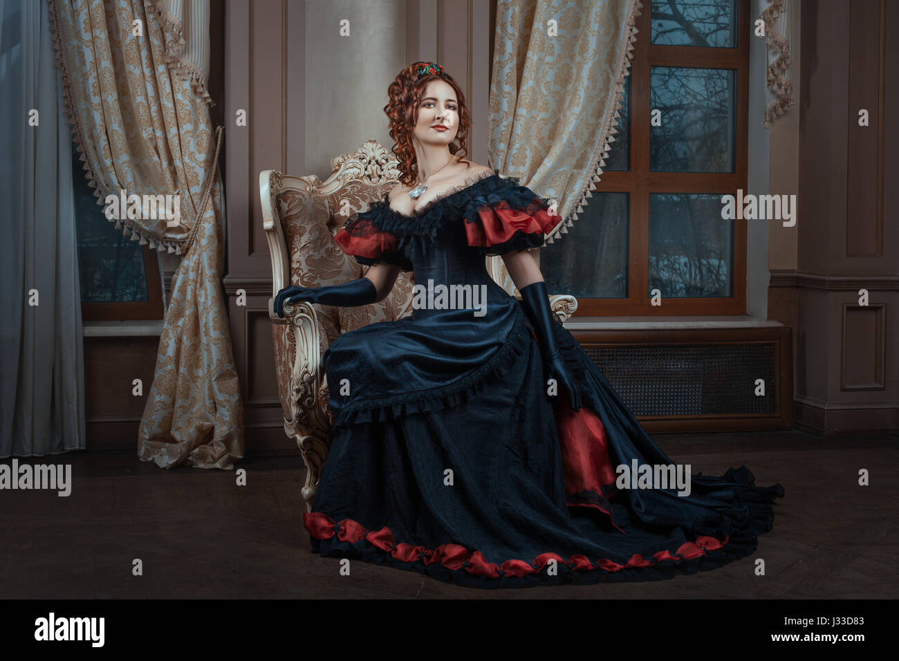 Frau im viktorianischen Kleid sitzt auf einem Stuhl im Zimmer. Stockfoto