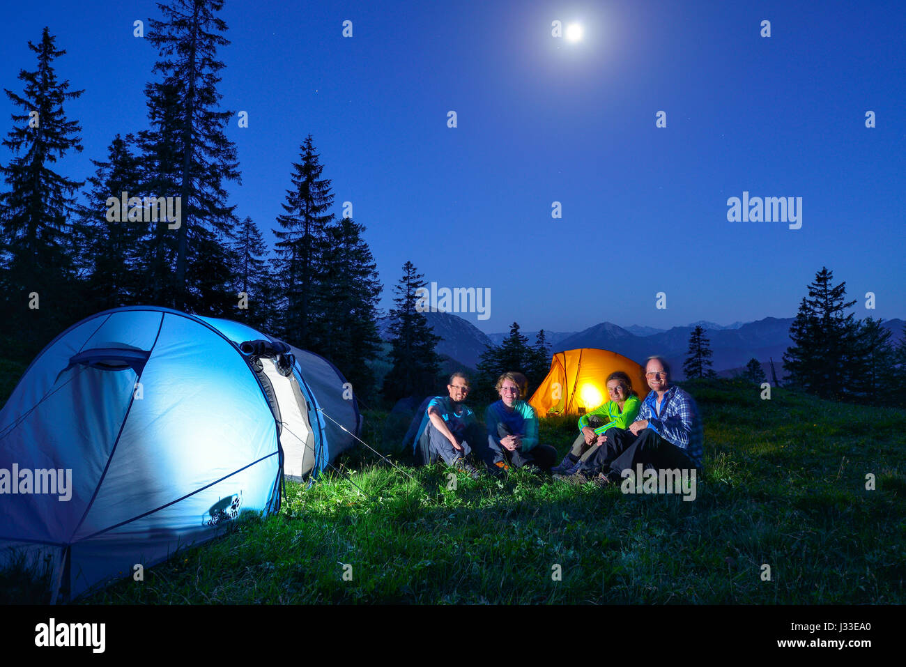 Vier Personen sitzen vor zwei beleuchtete Zelte, Blauberge, Bayerische Voralpen, Upper Bavaria, Bavaria, Germany Stockfoto