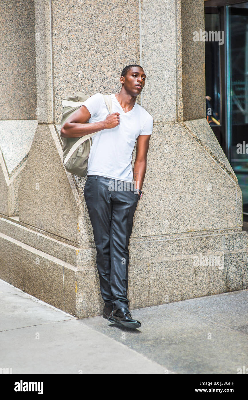 Street Fashion. Young African American Mann trägt weiße V Neck T Shirt, schwarze Hose, Lederschuhe, Schulter-Tragetasche, draußen, Büro bu Stockfoto