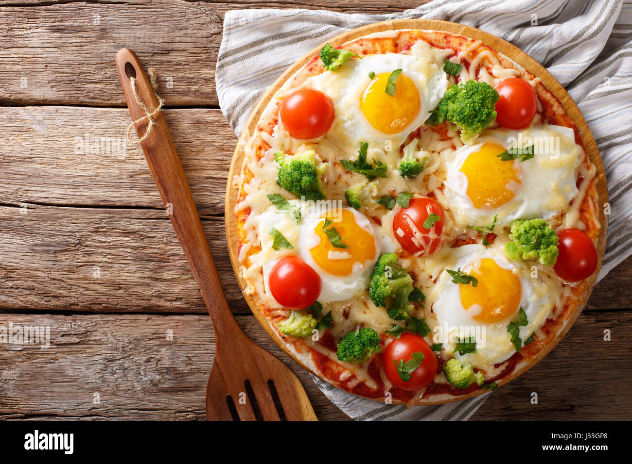 Pizza mit Eiern, Käse, Brokkoli, Tomaten und Kräutern Nahaufnahme auf dem Tisch. horizontale Ansicht von oben Stockfoto