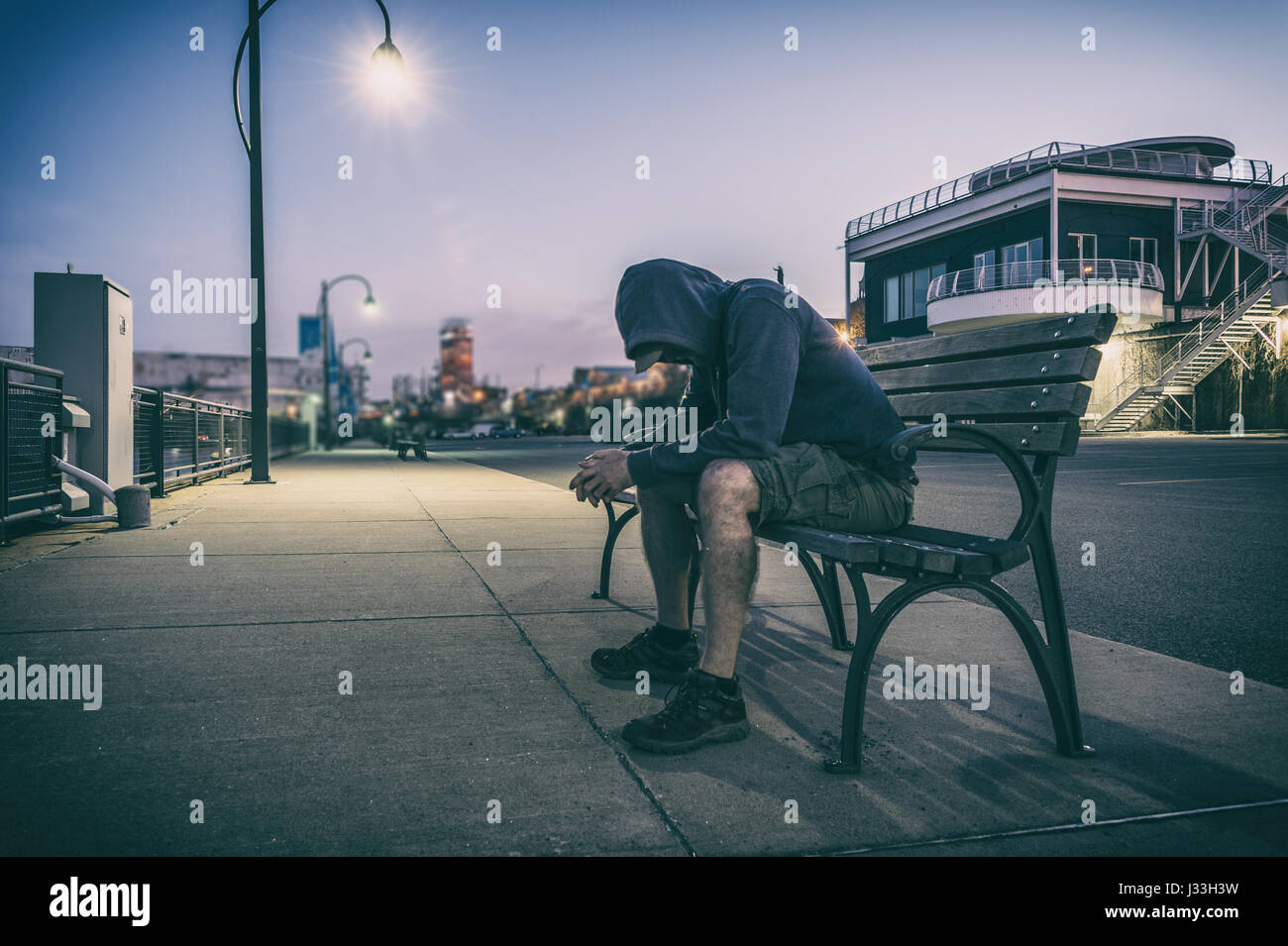 Traurig und einsam Mann mit versteckten Gesicht sitzen auf einer Bank bei Sonnenuntergang Stockfoto