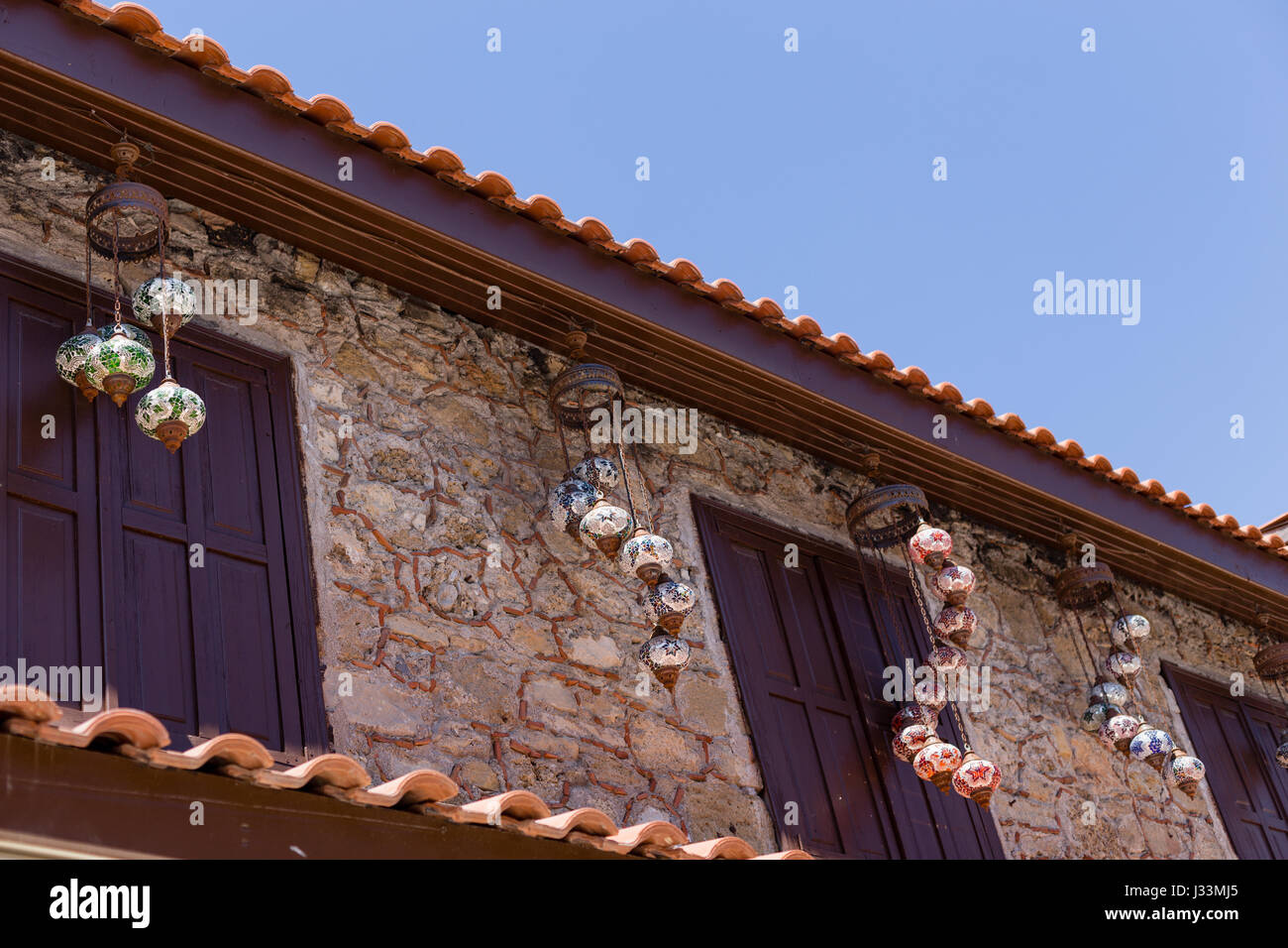 Horizontale Schuß von der oberen Etage des schönen alten Haus aus Stein mit dunkelbraunen Holz- Fenster shuttres und mehrere traditionelle türkische hängenden mosaiс lant Stockfoto