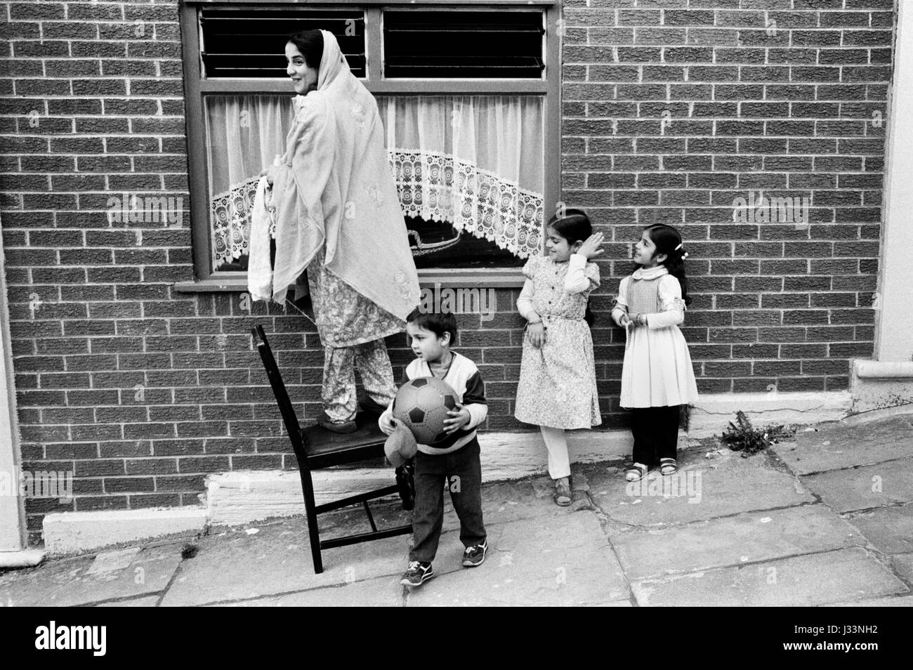 Schwarz Britisch asiatisch muslimische Familie Mutter und Kinder Jungen und Mädchen 1980s UK Sie putzt ihre Fenster. Blackburn Lancashire 1983 HOMER SYKES Stockfoto