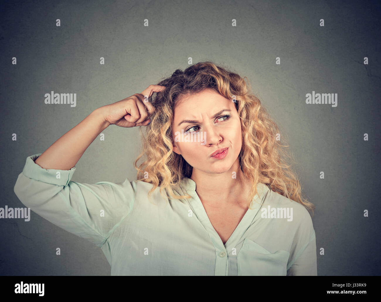 Junge Frau kratzen Kopf, auf grauem Hintergrund isoliert denken Tagträumen über etwas nachschlagen. Menschlichen Gesichtsausdruck Emotion Gefühl Stockfoto