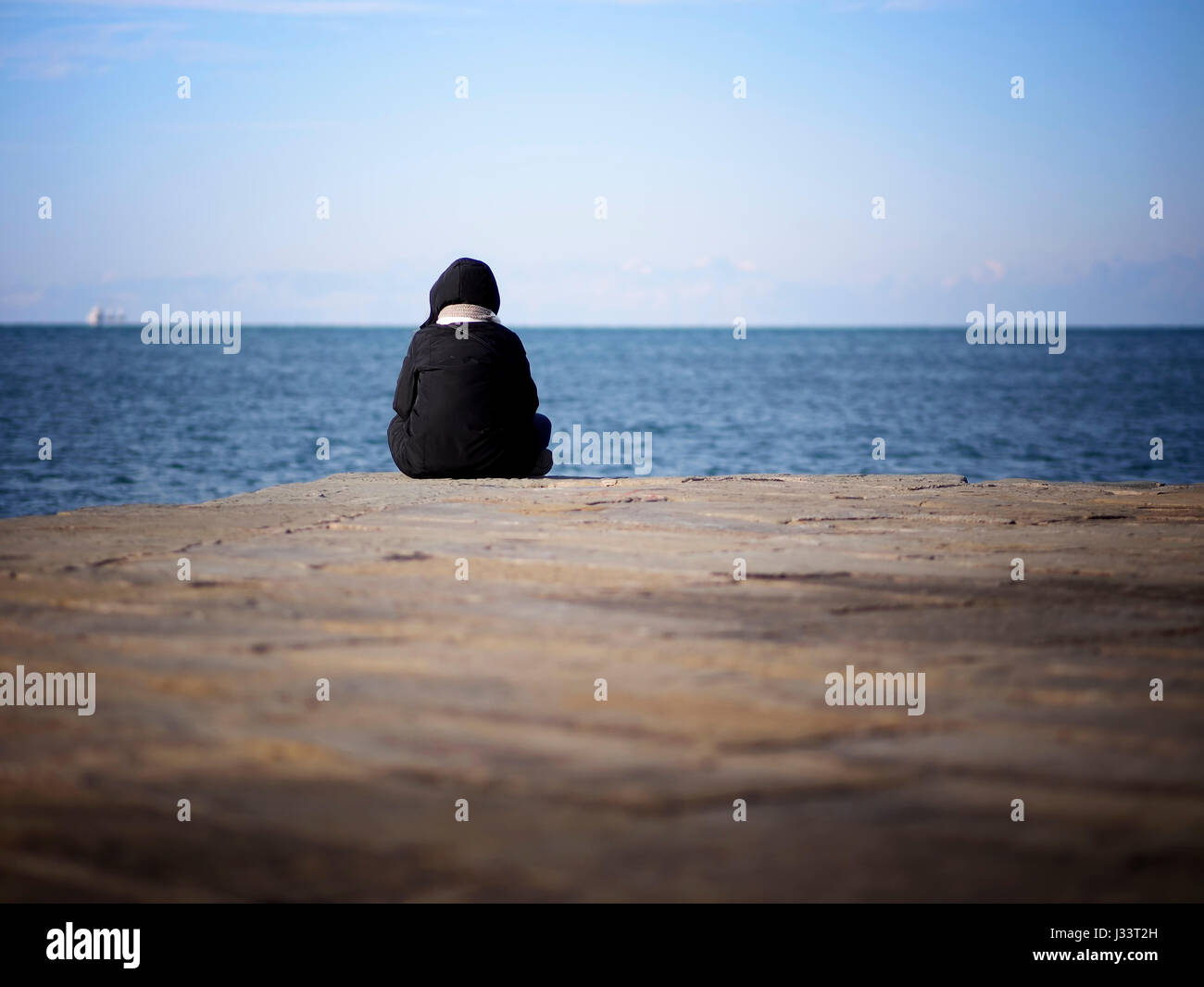 Eine Person sitzt am Ende eines Piers in einem kalten Morgen das Meer genießen. Stockfoto