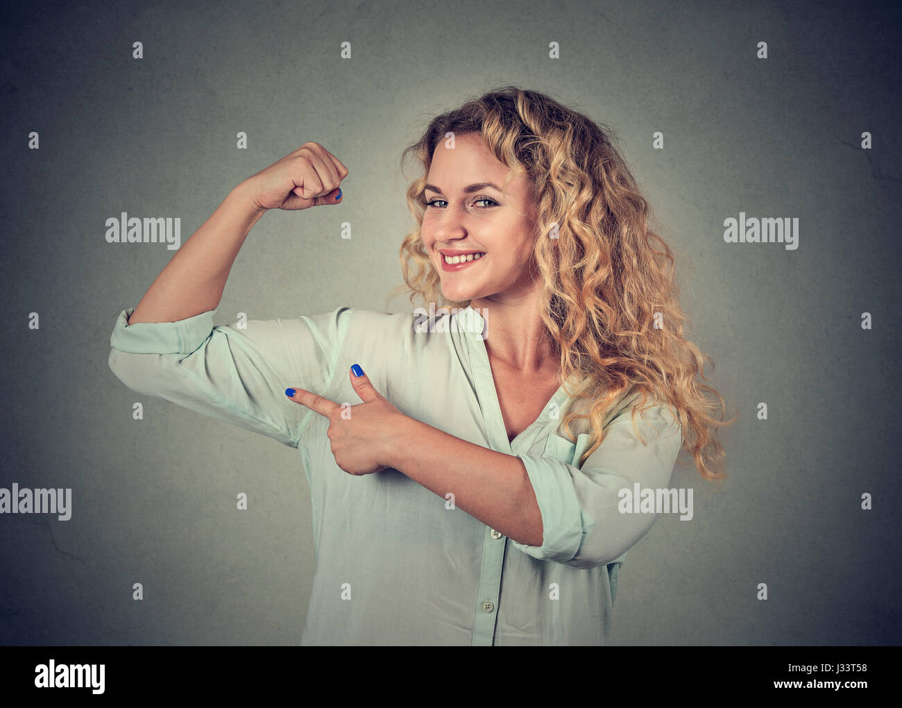 Closeup Portrait junge glückliche Frau Muskeln zeigen ihre Stärke auf graue Wand Hintergrund isoliert. Positive Emotionen Gesichtsausdruck Gefühl. Stockfoto