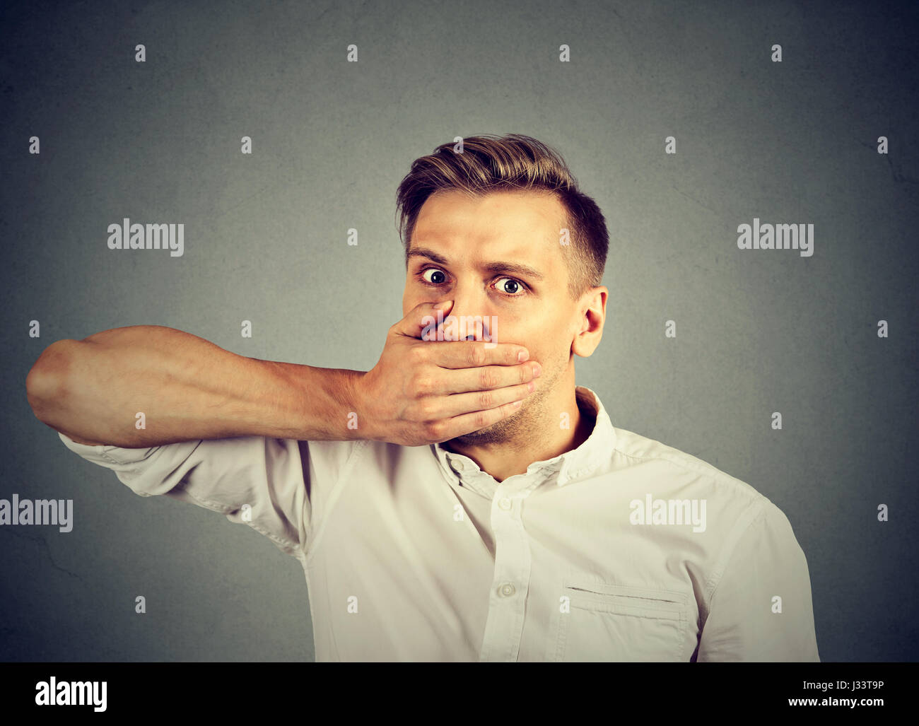 Angst, jungen Mann, den Mund mit der Hand auf graue Wand Hintergrund isoliert. Menschliche Emotionen Gesichtsausdruck Stockfoto