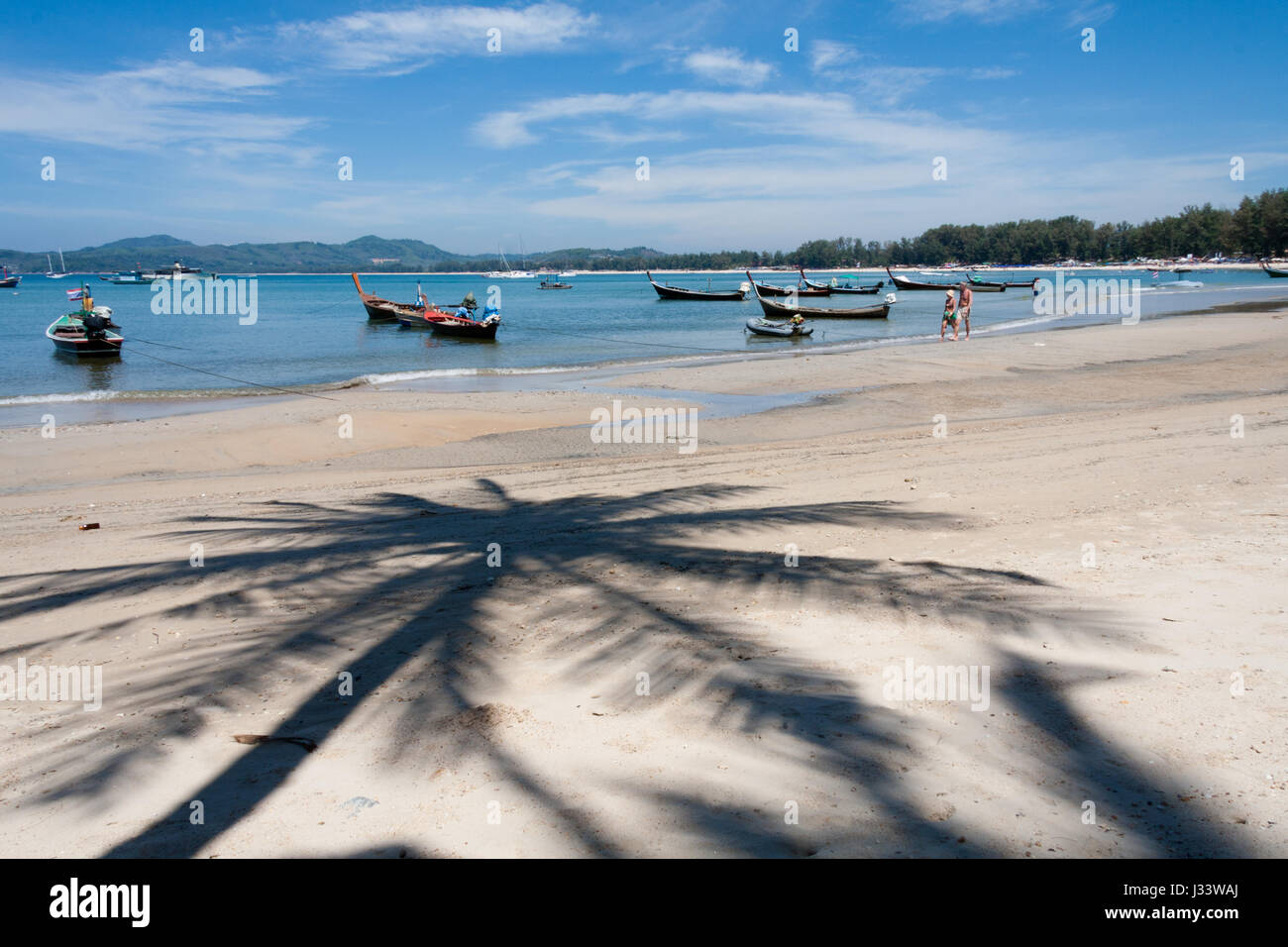 Menschen zu Fuß auf den Strand, vorbei an Boote mit Palme Baum Schatten, Bang Tao Beach, Phuket, Thailand Stockfoto