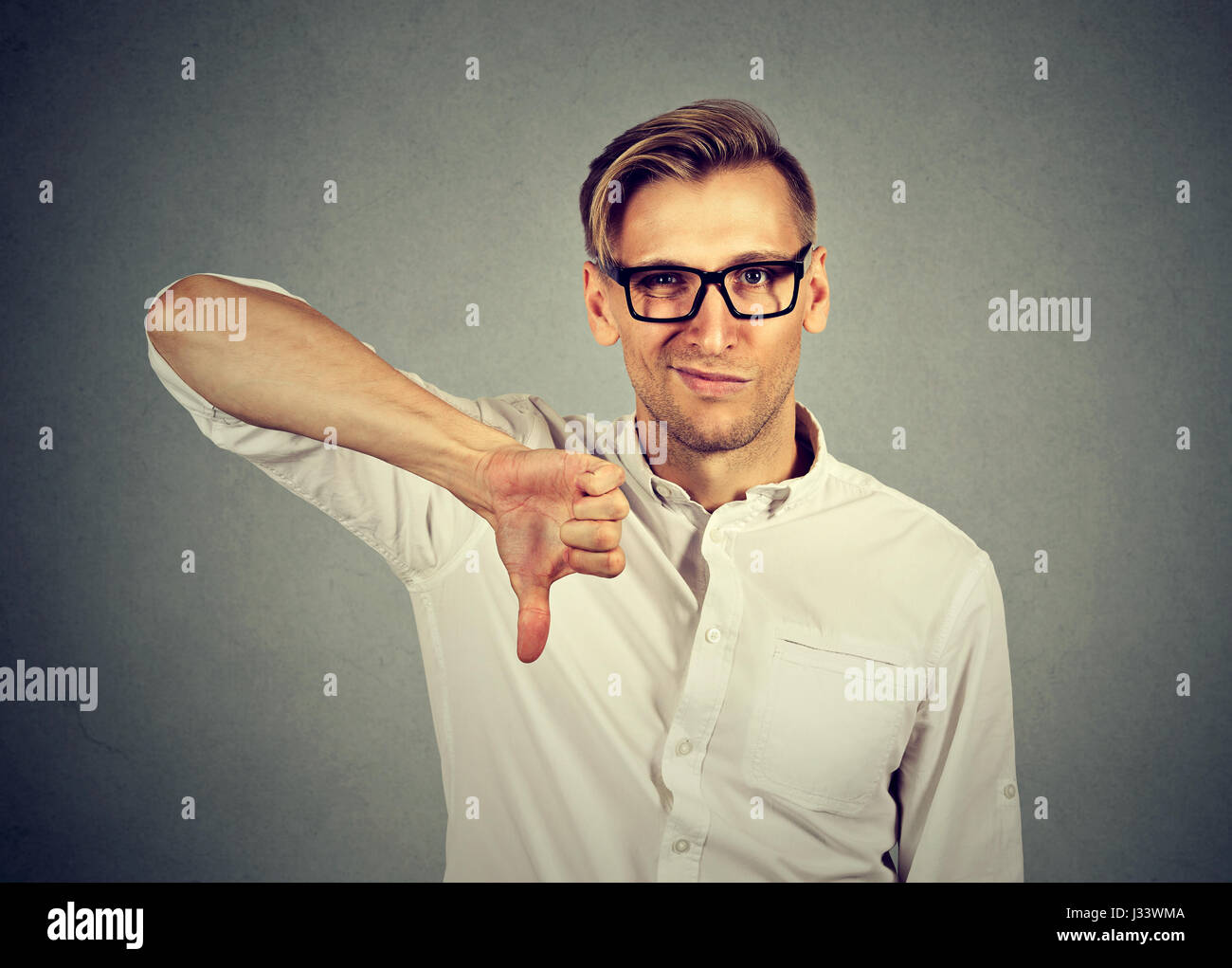 wütend, unglücklich, junger Mann mit Daumen runter-Zeichen, in Ablehnung des Angebots auf grauem Hintergrund isoliert. Negative menschliche Emotion Gesichtsausdruck fühlen Stockfoto