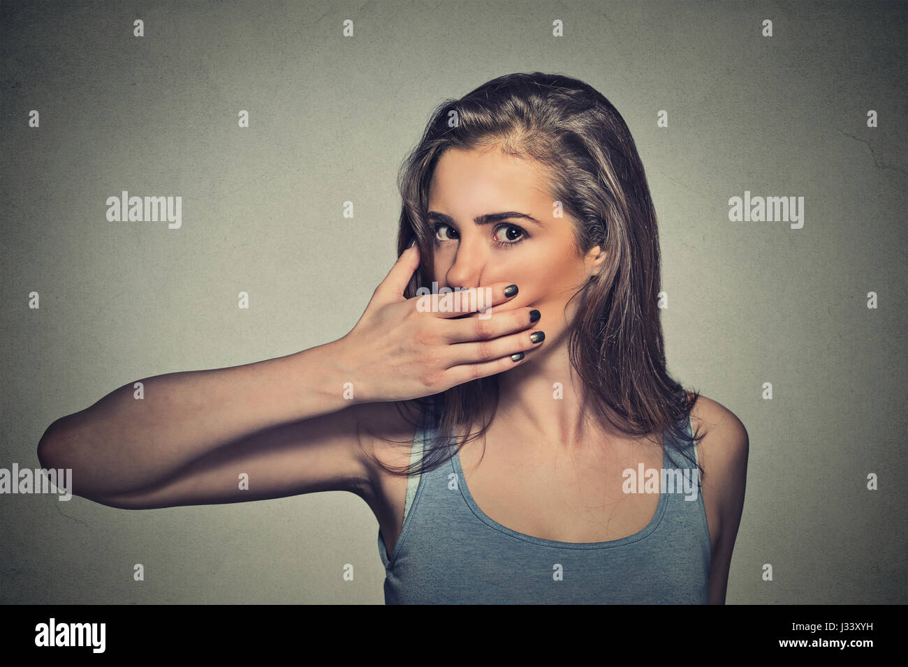 Closeup Portrait von Angst, junge Frau, die den Mund mit der Hand ihr auf graue Wand Hintergrund isoliert Stockfoto