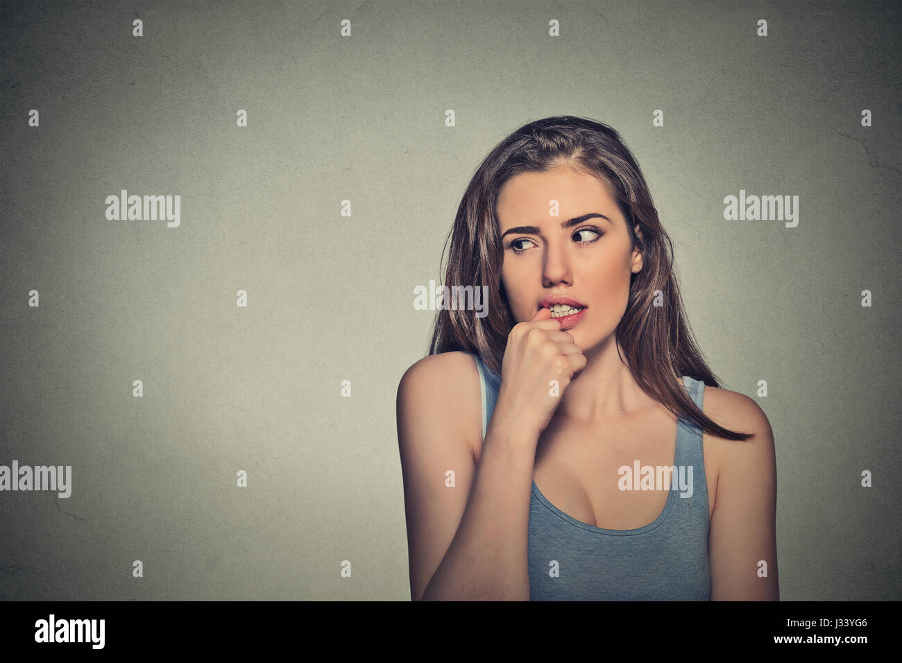 Closeup Portrait nervös suchen junge Frau beißen ihre Fingernägel verlangen etwas ängstlich isoliert textfreiraum grau hinterlegt. Negativen menschlichen emot Stockfoto