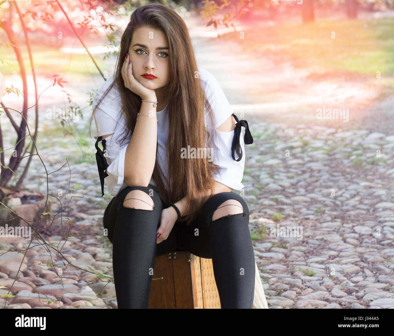 Schöne junge Frau sitzt auf Reisekoffer Blick in die Kamera Stockfoto