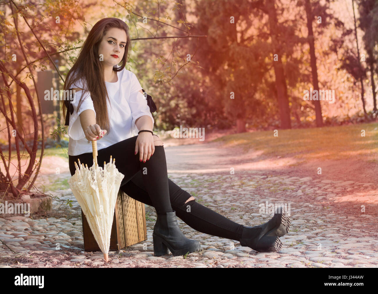 In voller Länge Portrait von junge Frau sitzt auf Vintage Koffer mit einem Regenschirm. Stockfoto