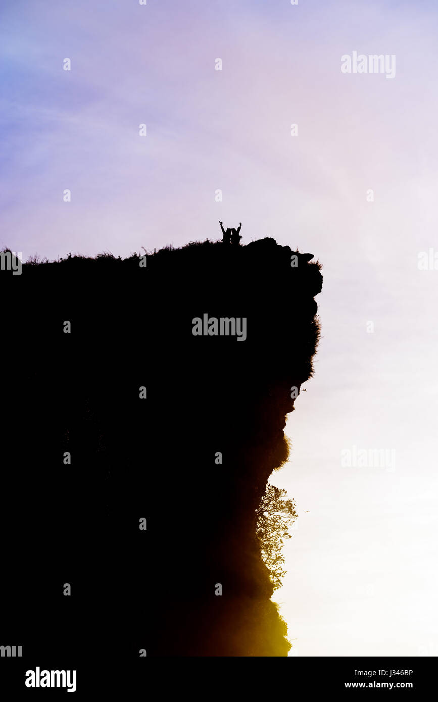 Schwarze Silhouette am Himmelshintergrund von zwei touristischen stehend Arme ausgestreckt zufrieden mit Erfolg am Spitzberg in der Nähe der Klippe bei Sonnenaufgang an Phu Stockfoto