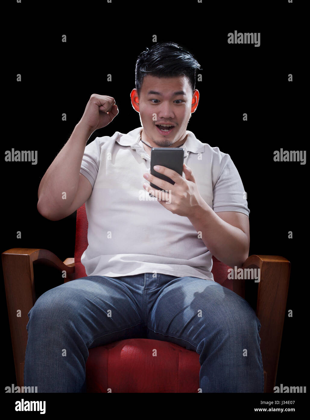man sitzt auf Sessel und beobachtete an Smartphone mit spannenden Gesicht Stockfoto