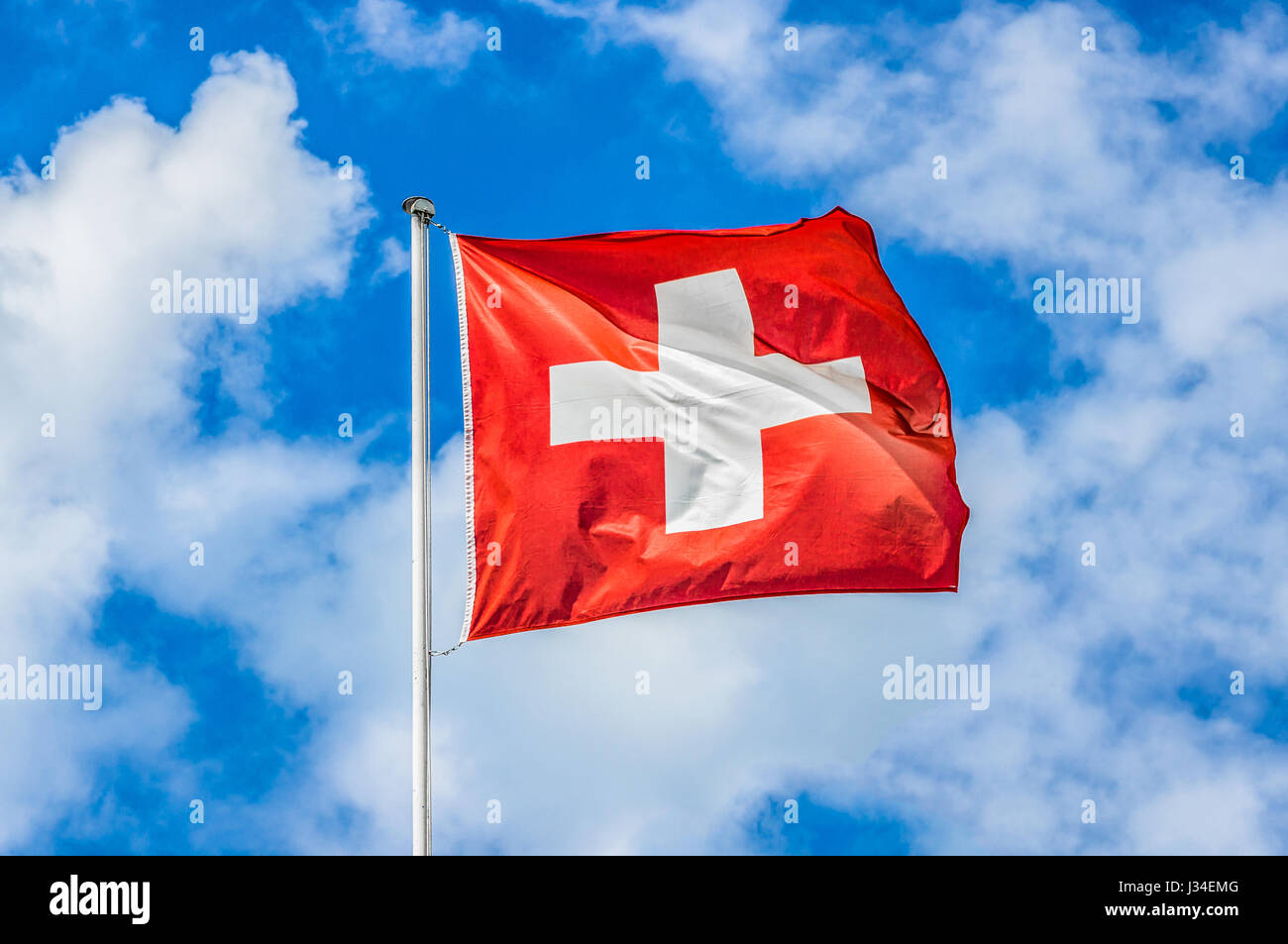 Klassische Ansicht der Nationalflagge der Schweiz winken in den Wind gegen blauen Himmel und Wolken an einem sonnigen Tag im Sommer Stockfoto