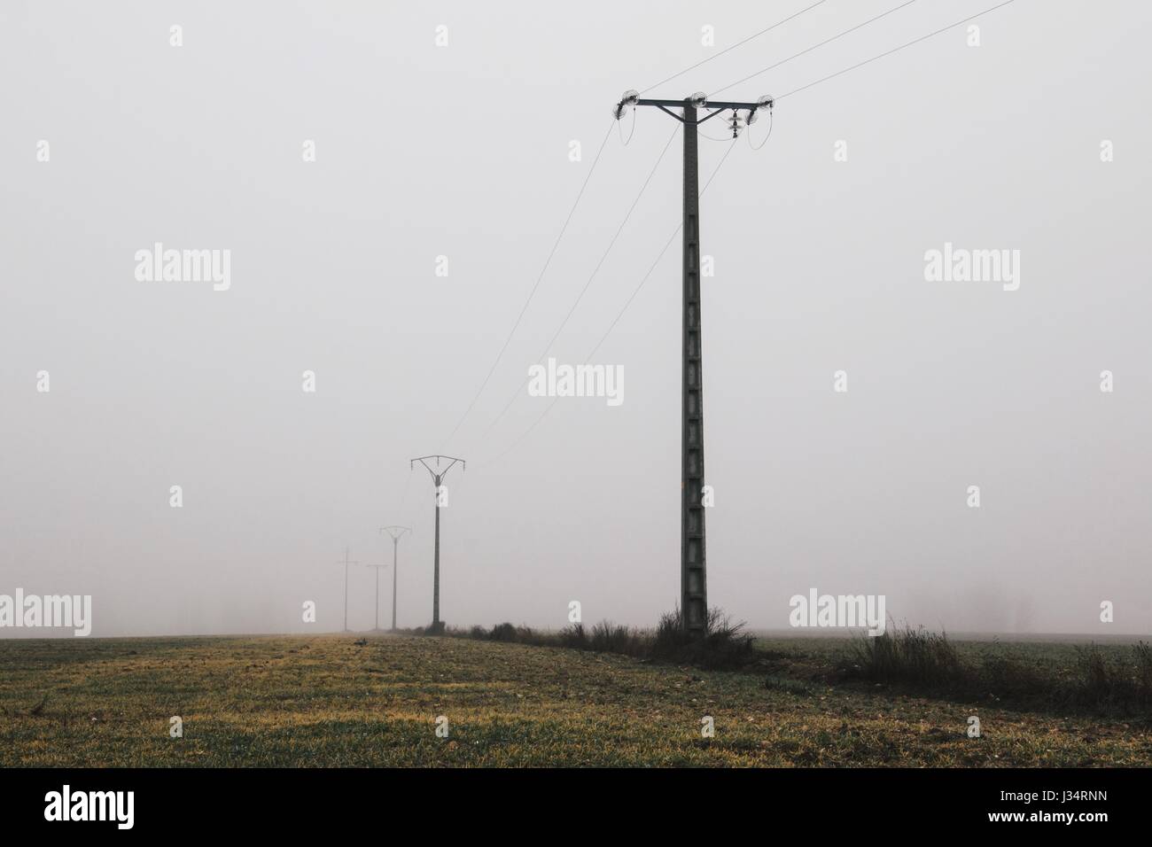 Elektrische Leitungen in der spanischen Landschaft über den gefrorenen Ernte-Feldern in einem nebeligen Wintertag Stockfoto