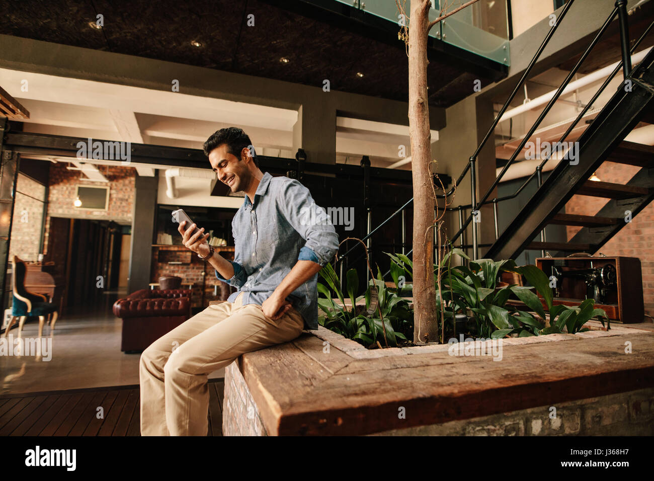 Seitenansicht der glücklicher junge Mann sitzen im modernen Büro lesen SMS auf seinem Handy und lächelnd. Kreative Geschäftsmann mit Smartphone-dur Stockfoto