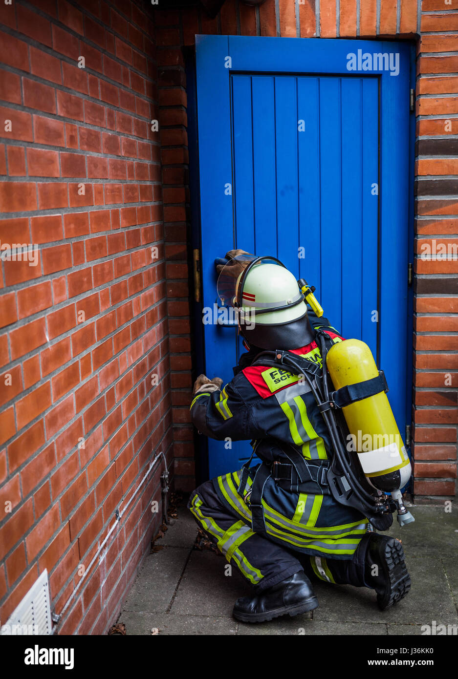 Feuerwehrmann öffnet eine Tür in Aktion mit Sauerstoffflasche und Atemschutz Maske - HDR Stockfoto