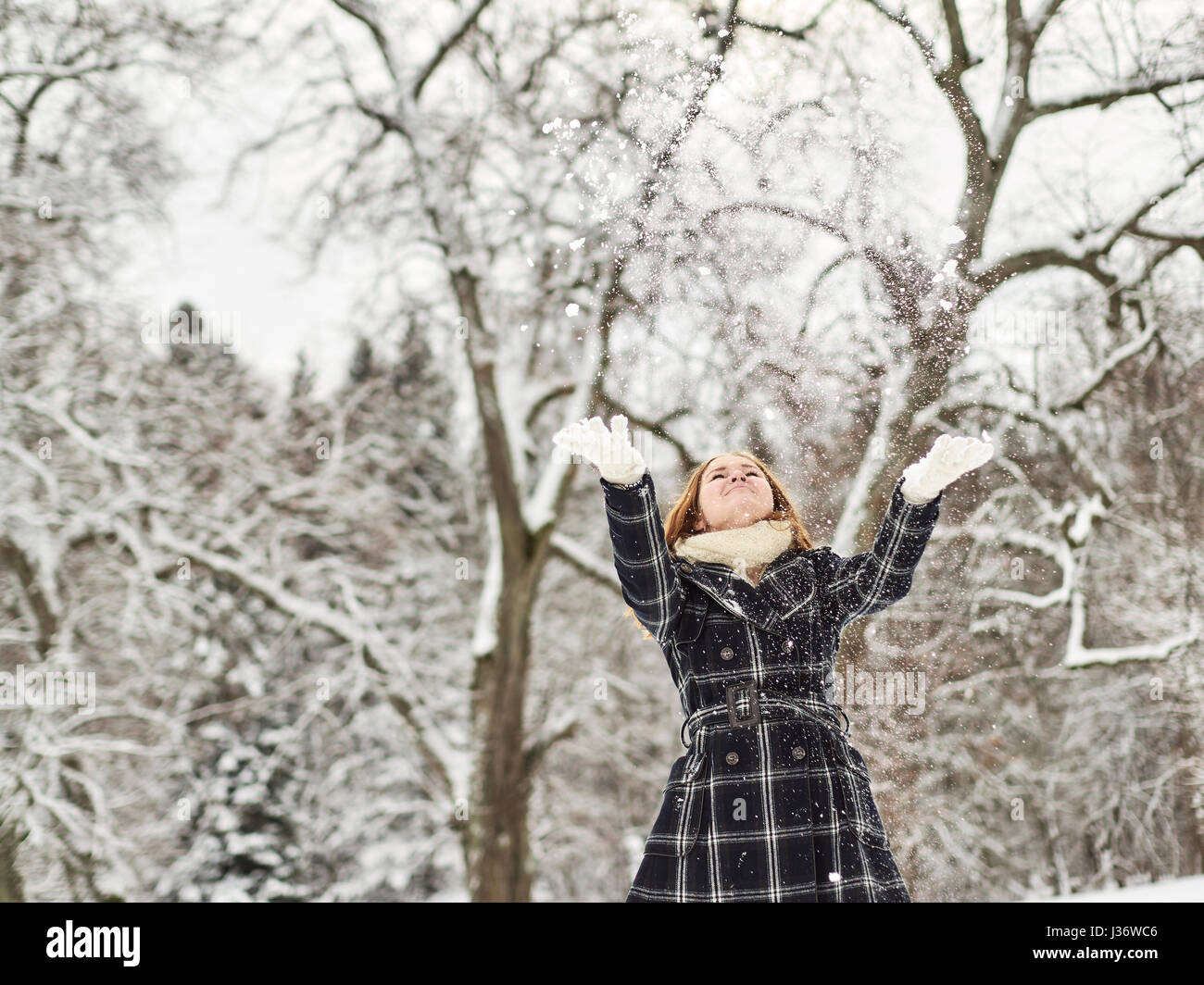 Schöne junge Mädchen tragen einen Wintermantel und kotzte Schnee in der Luft, Finnisch Wintertag im Februar Stockfoto